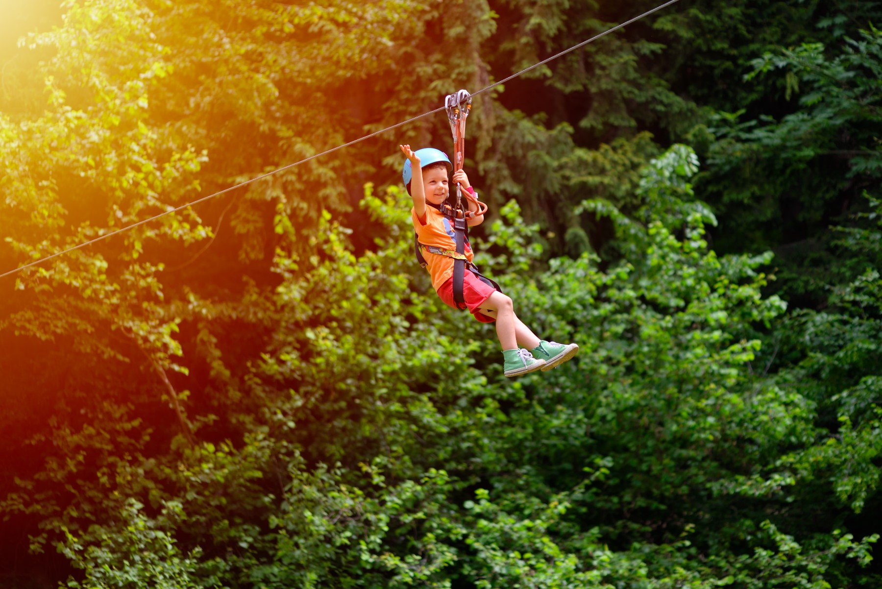 Happy kid with helmet and harness on zip line between trees
